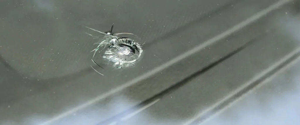 An image showing a car's windshield with a visible bullet hole, indicating damage caused by a firearm.